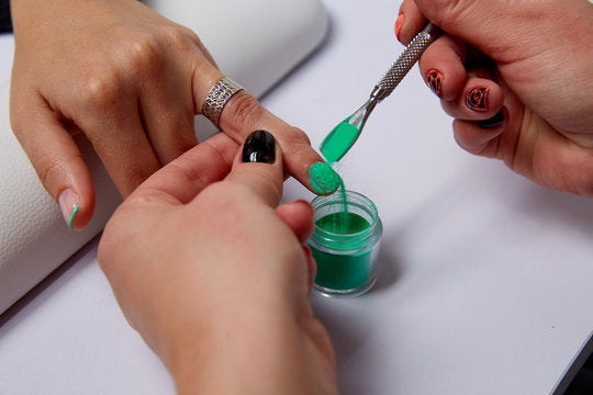 Groene gel nagellak wordt met een metalen spatel uit een glazen potje gehaald voor dipping powder nagels voordelen