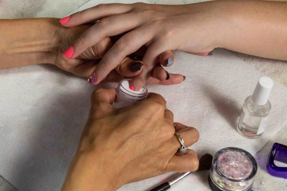 Een hand houdt een klein helder potje met roze glitter dipping powder voor nagels in de ultieme gids.