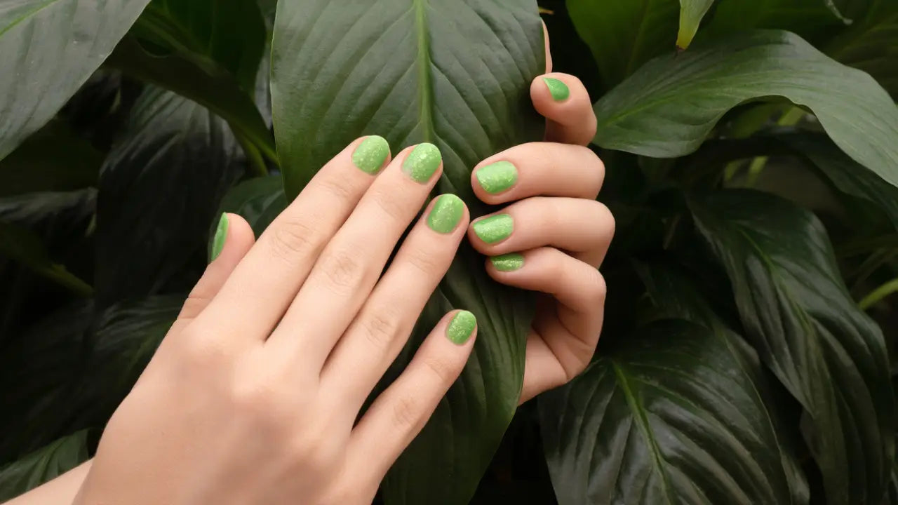 Handen met glanzende groene nagellak die een groot donkergroen blad voorzichtig vasthouden bij verkleurde natuurlijke nagels