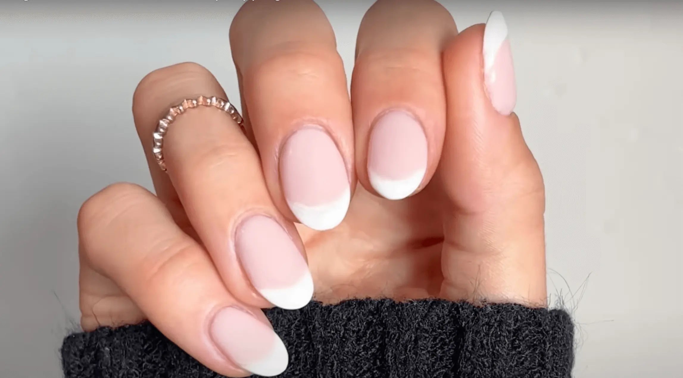 Een hand met elegant gemanicuurde nagels in zachte roze french tip en een fijne roségouden ring aan de ringvinger