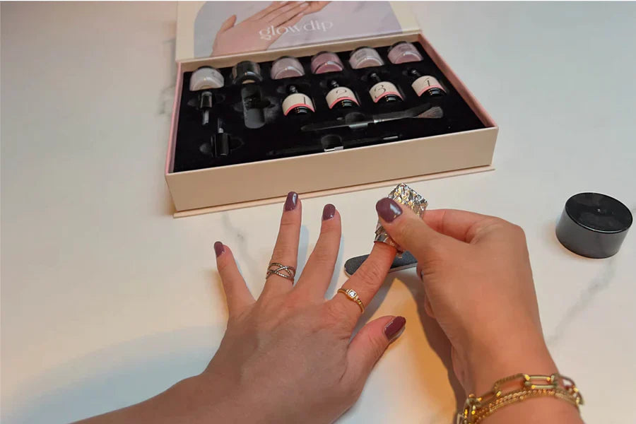 Een paar handen met donkerpaarse poeder nagellak, één hand met gouden ringen en bijpassende armband