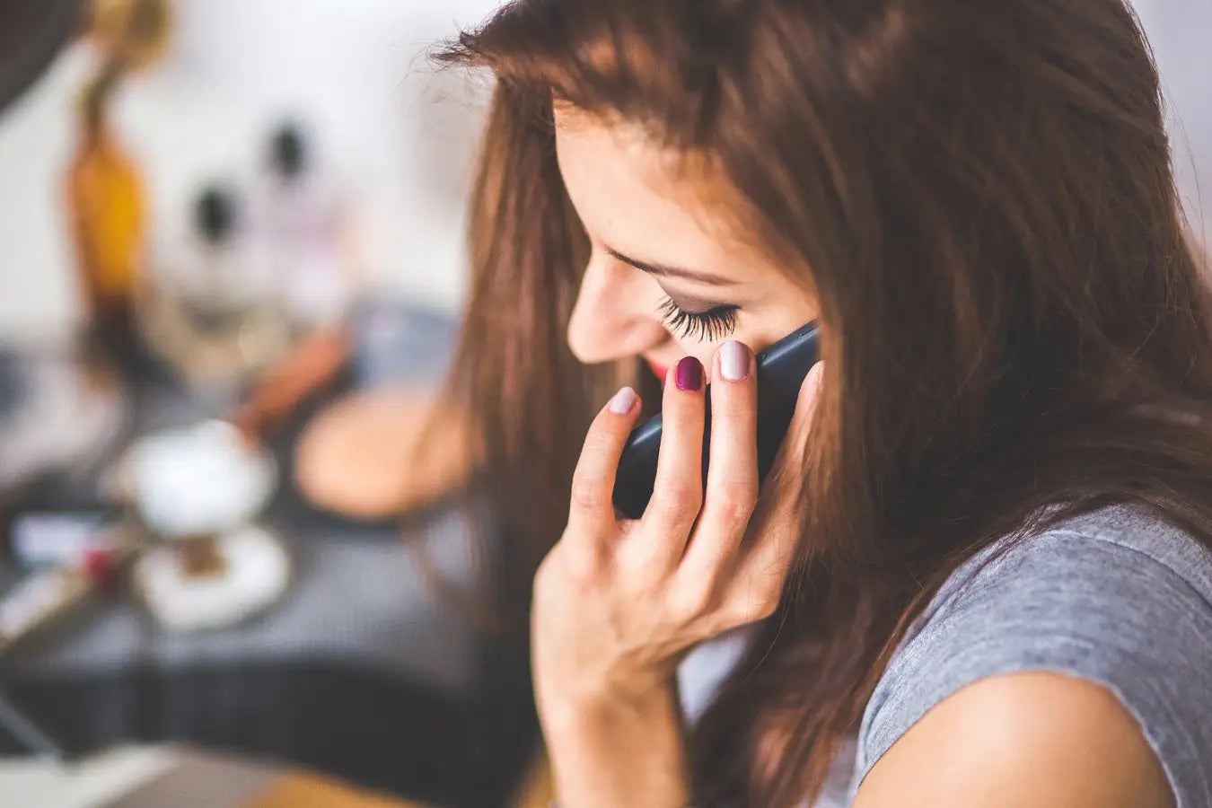 Vrouw met lang bruin haar houdt een zwarte smartphone met matte afwerking vast bij het oor in artikel over dip powder aanbrengen
