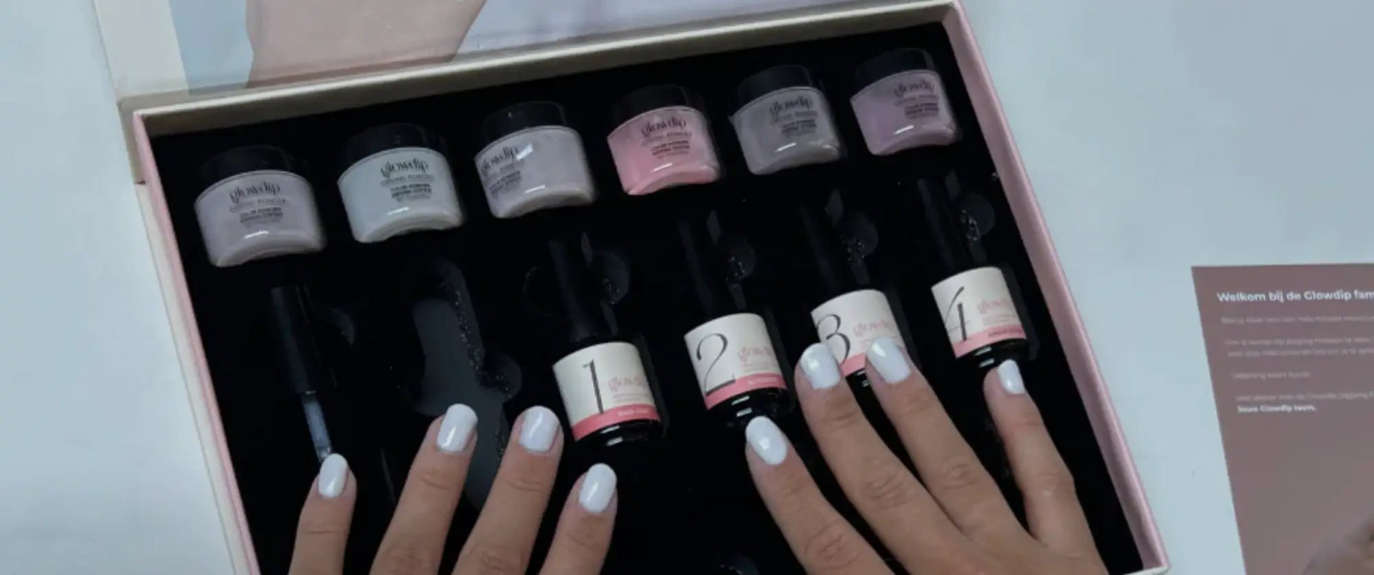 Een set van zes kleine cilindervormige nagellakflessen met zwarte doppen en roze accenten in een roségouden doos