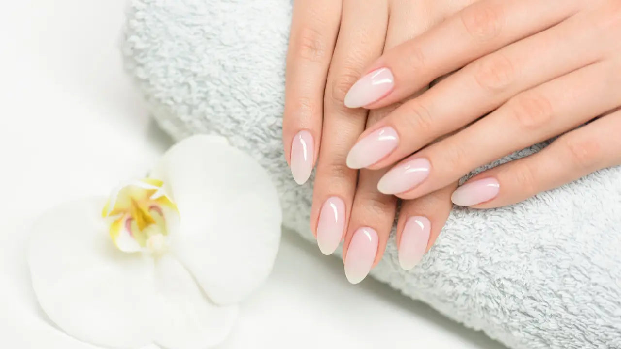 Handen met lange amandelvormige nagels in zachte nude kleur om broze nagels te verbeteren