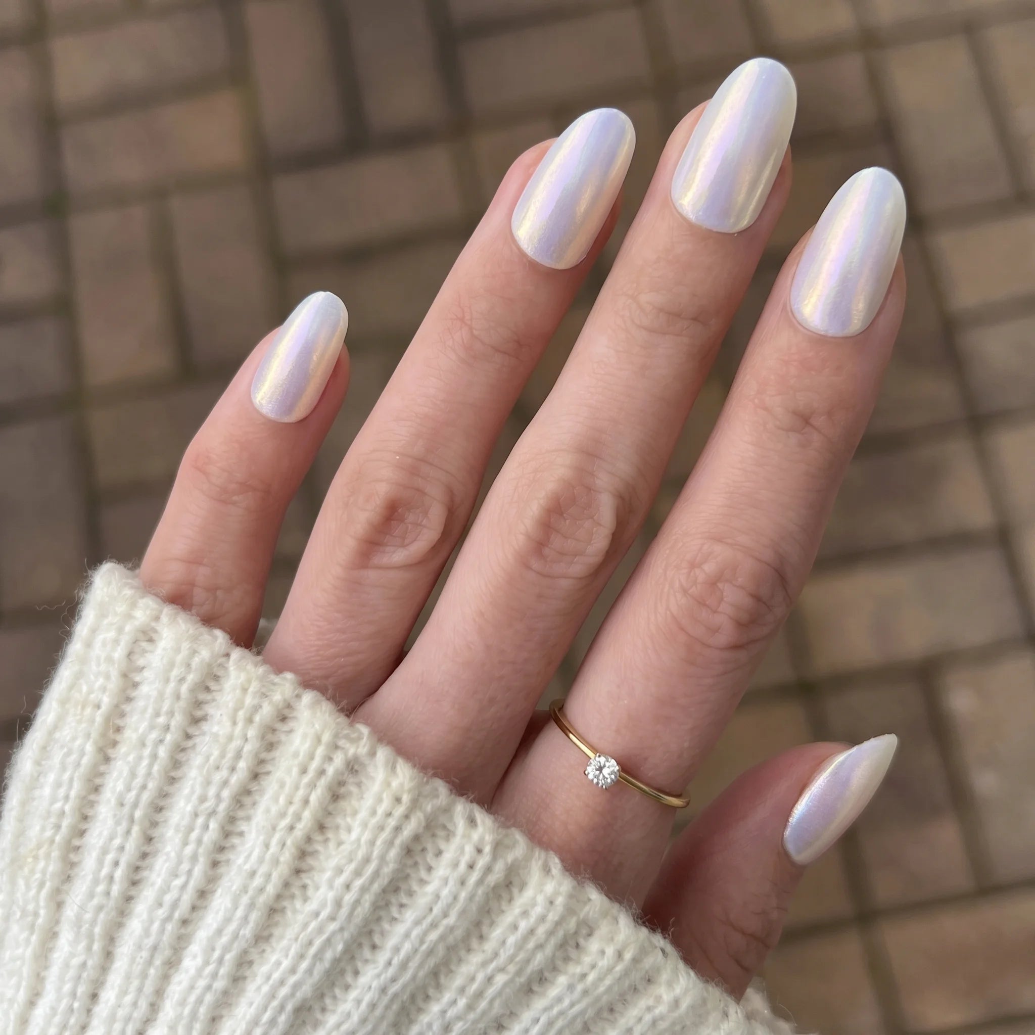 Hand met lange amandelvormige nagels in glinsterende witte holografische cosmic shift chrome poeder en gouden ring