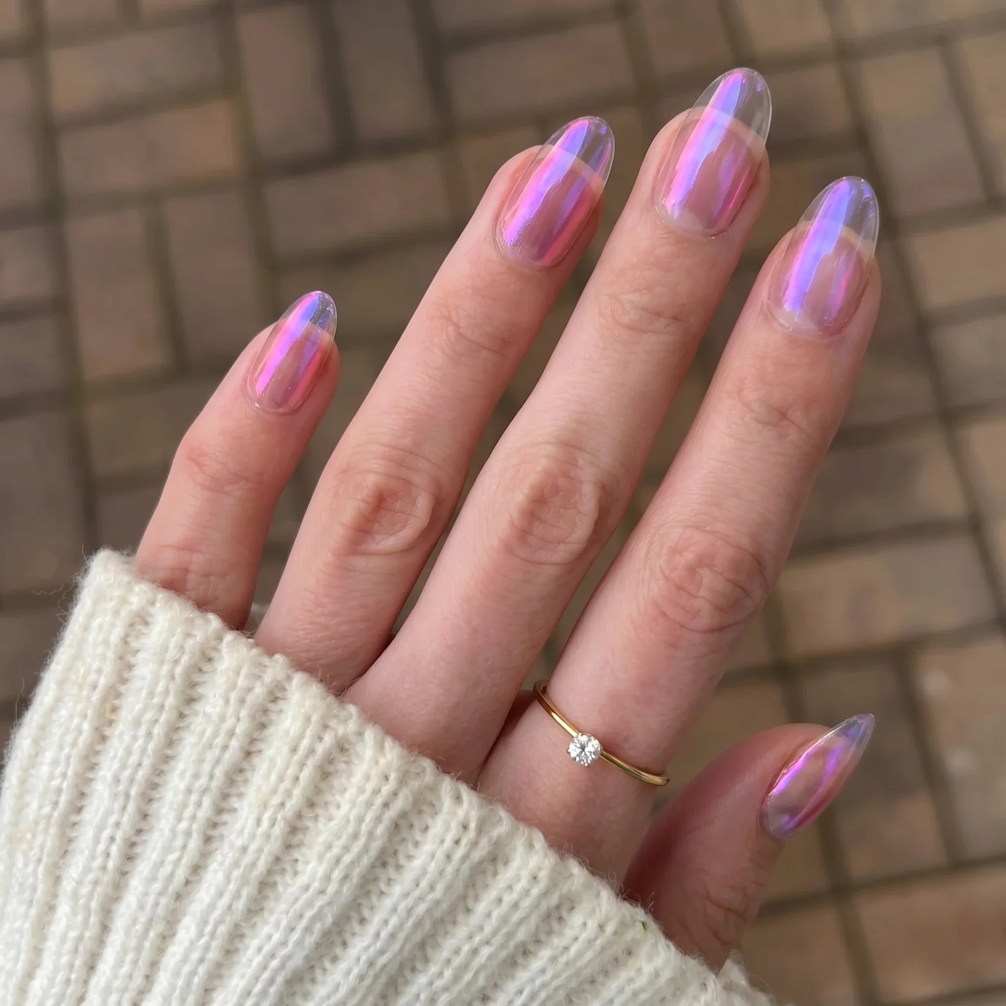 Hand met lange amandelvormige nagels met glinsterende holografische roze paarse finish van golden shift chrome powder