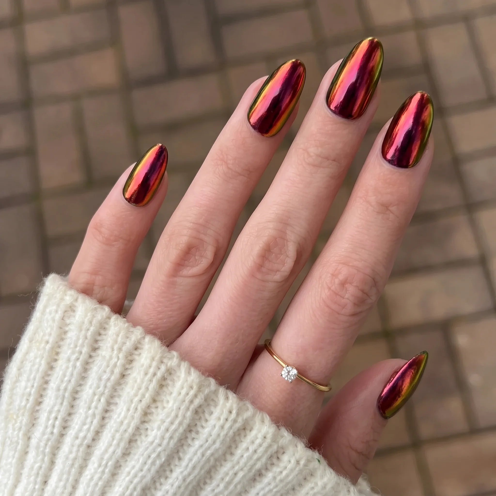 Vibrante iriserende rode en gouden crimson shift chrome powder nagellak met glanzende metalen afwerking op amandelvormige nagels