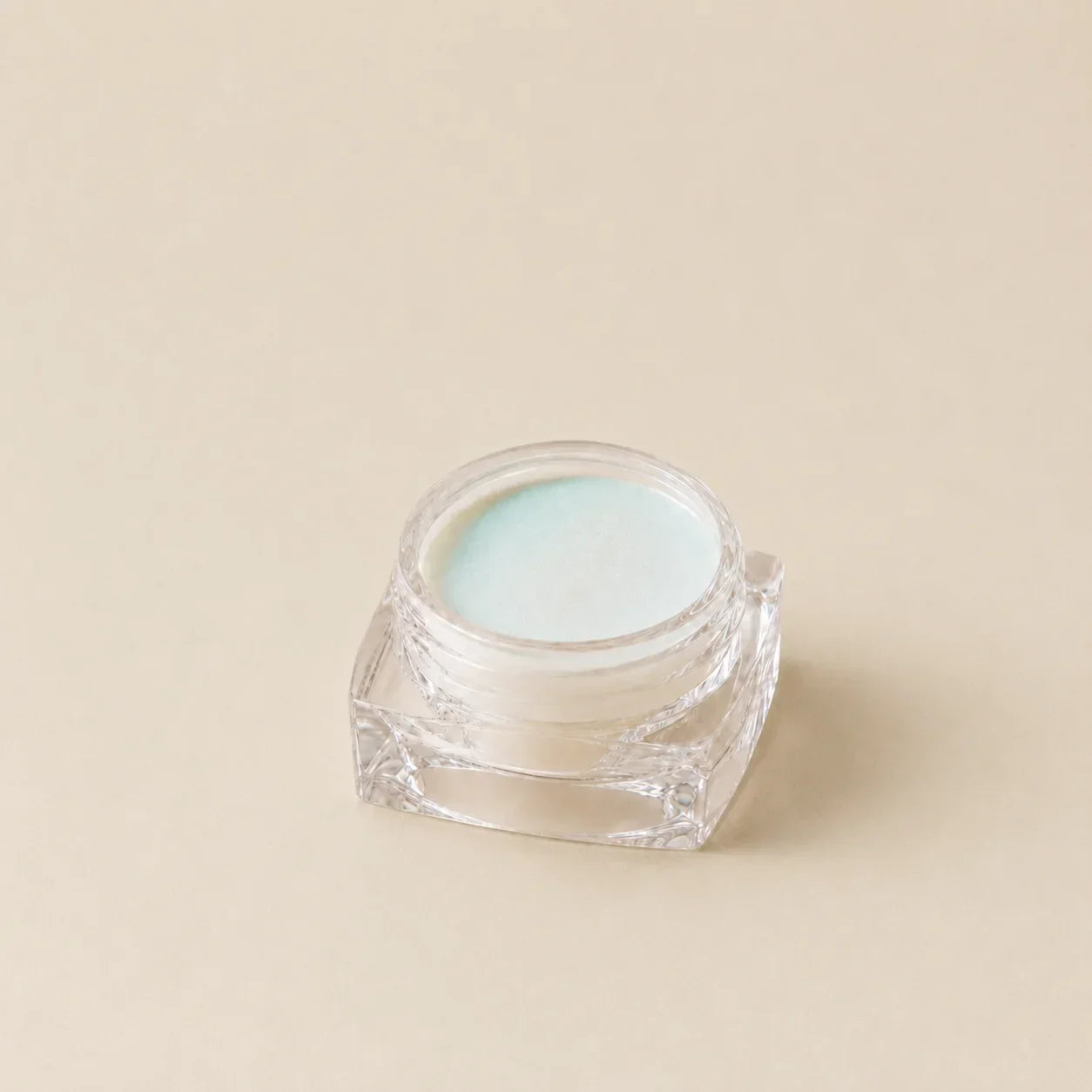 Een helder geslepen glazen pot met een glad, lichtblauw cosmetisch balsem in de chrome powder bundle met 5 kleuren