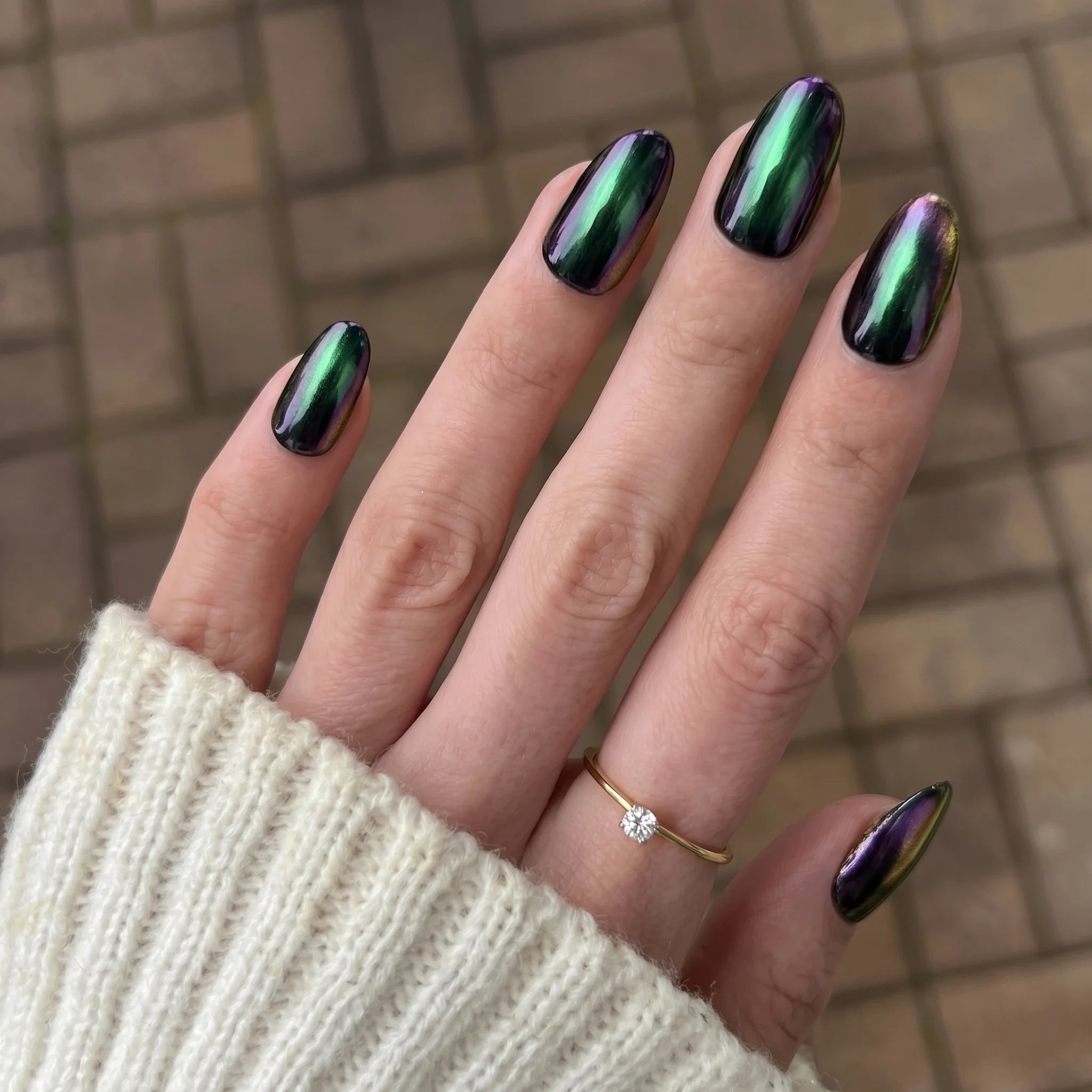 Hand met lange amandelvormige nagels gelakt met glanzende iriserende groene en paarse holografische golden shift chrome powder