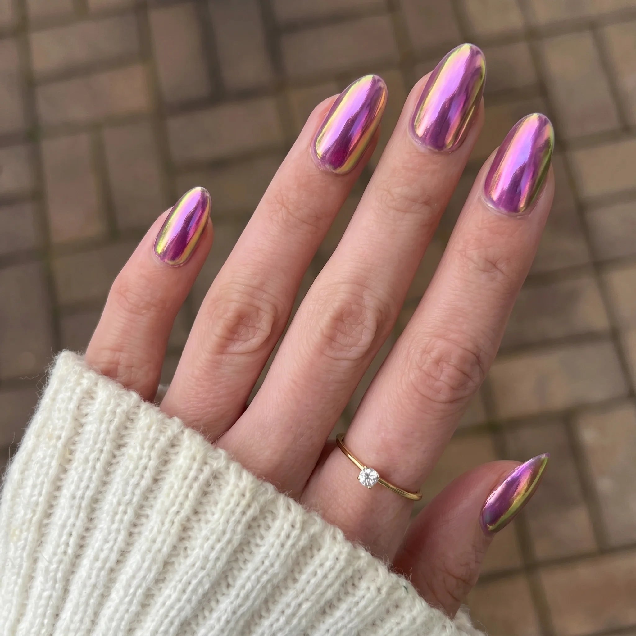 Hand met lange amandelvormige nagels in een glinsterende holografische paarse en gouden metallic finish met golden shift chrome powder