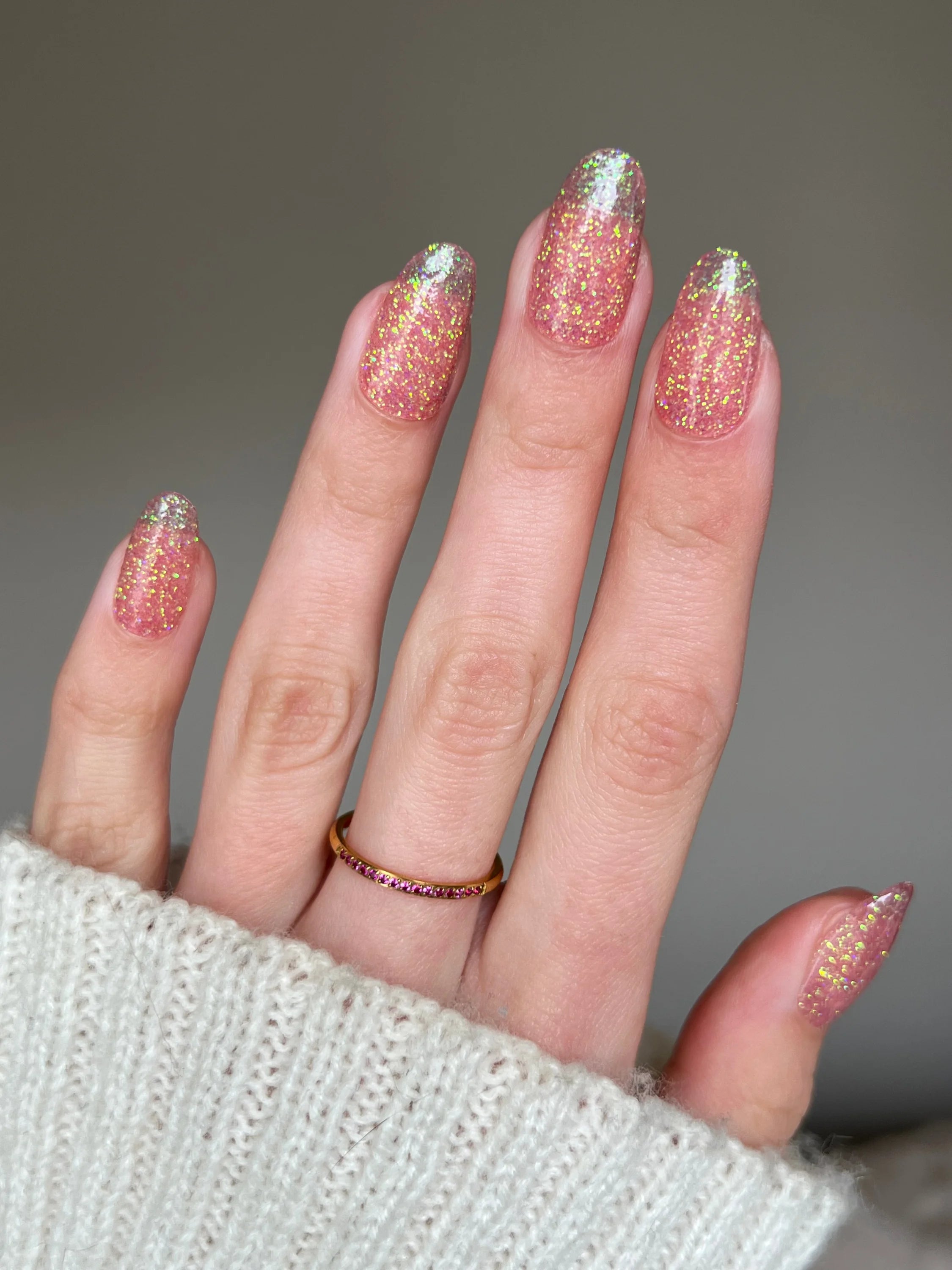 Een hand met lange amandelvormige nagels gelakt met glinsterende rosegoud glitter dipping powder en een delicate ring